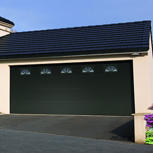Porte de garage au panneau nervuré vert foncé.
Option : hublots rectangulaires au motif rayon de soleil, encadrement PVC.